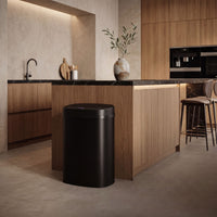 Bayt sensor prullenbak van 60 liter in mat zwart naast een houten keukeneiland in een warm, modern interieur